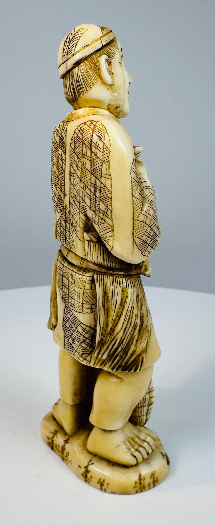 Side view of a Japanese carved fisherman standing barefoot on an oval base
