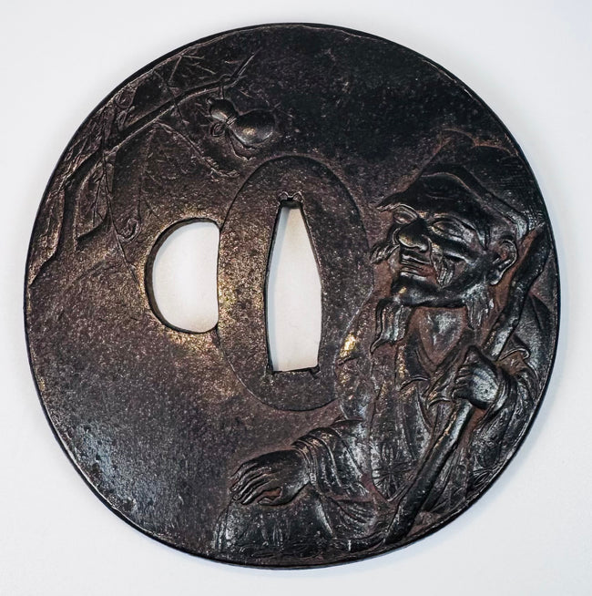 Front view of an antique Japanese tsuba depicting a bearded sage with staff and a spider among tree branches