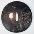 Front view of an antique Japanese tsuba depicting a bearded sage with staff and a spider among tree branches
