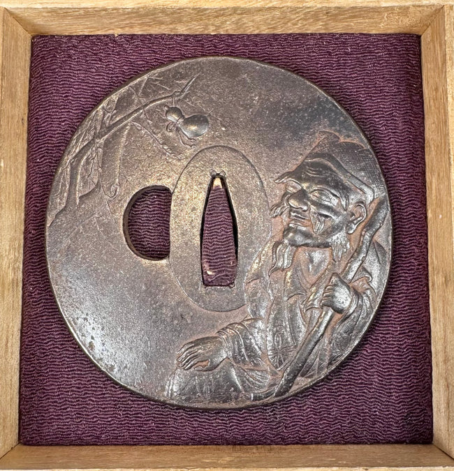 Angled view of a circular Japanese iron sword guard with an elderly sage beneath a spider in tree branches