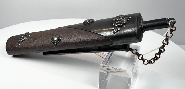 Angled rear view of antique Japanese gunpowder flask showing suspension clip, textured lacquered body and metal fittings