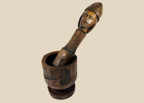 18th–19th Century European wooden mortar and pestle, featuring a finely carved human face on the pestle. The robust mortar and intricately detailed pestle showcase traditional craftsmanship, rich patina, and centuries of use, reflecting both utilitarian function and cultural artistry.