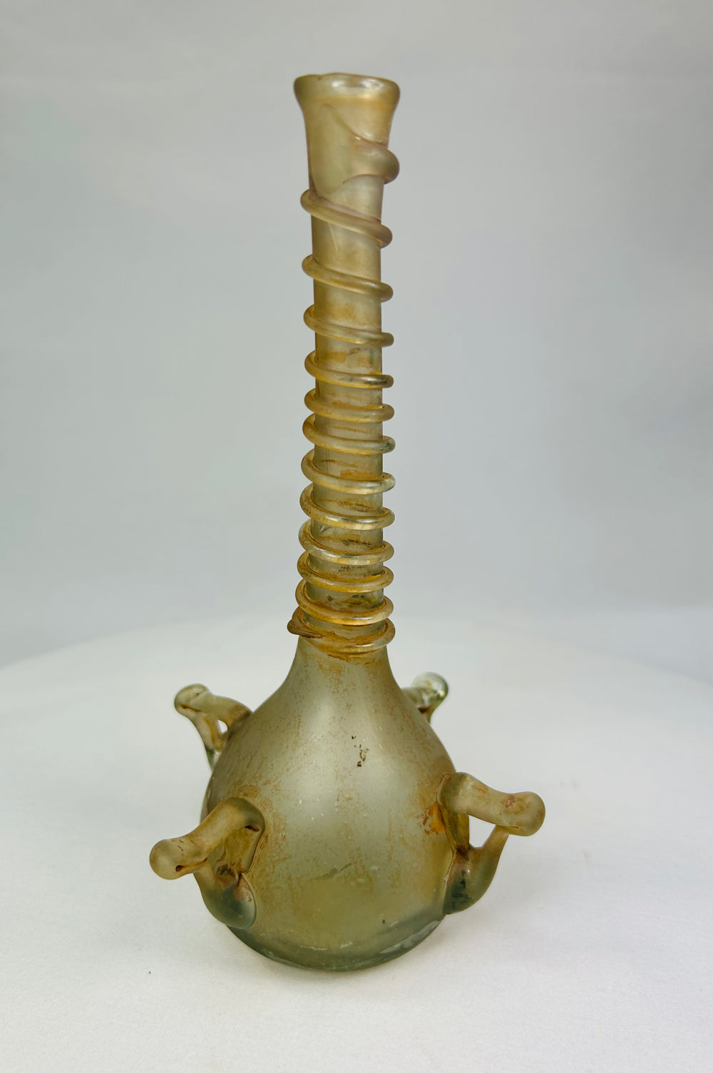 Ancient Islamic glass bottle featuring a spiral-threaded neck and applied loop handles, displayed on a white background.