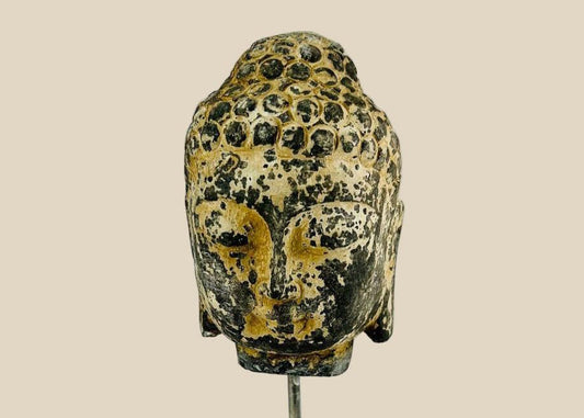 Antique carved stone Buddha head from Southeast Asia, likely Thailand or Cambodia, 18th–19th Century. Features serene meditative expression, curled hair, and traces of original pigments. Mounted on a marble base, reflecting Buddhist artistry, spiritual symbolism, and historical craftsmanship of the region.