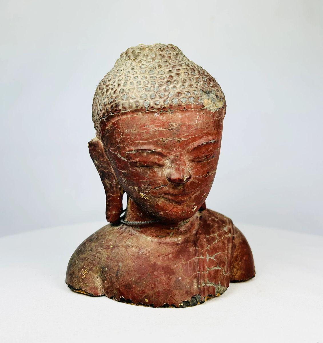 19th-century Southeast Asian wooden Buddha bust, likely Thailand or Burma, with serene features, red lacquer, gold gilt remnants, and metal chain detail.