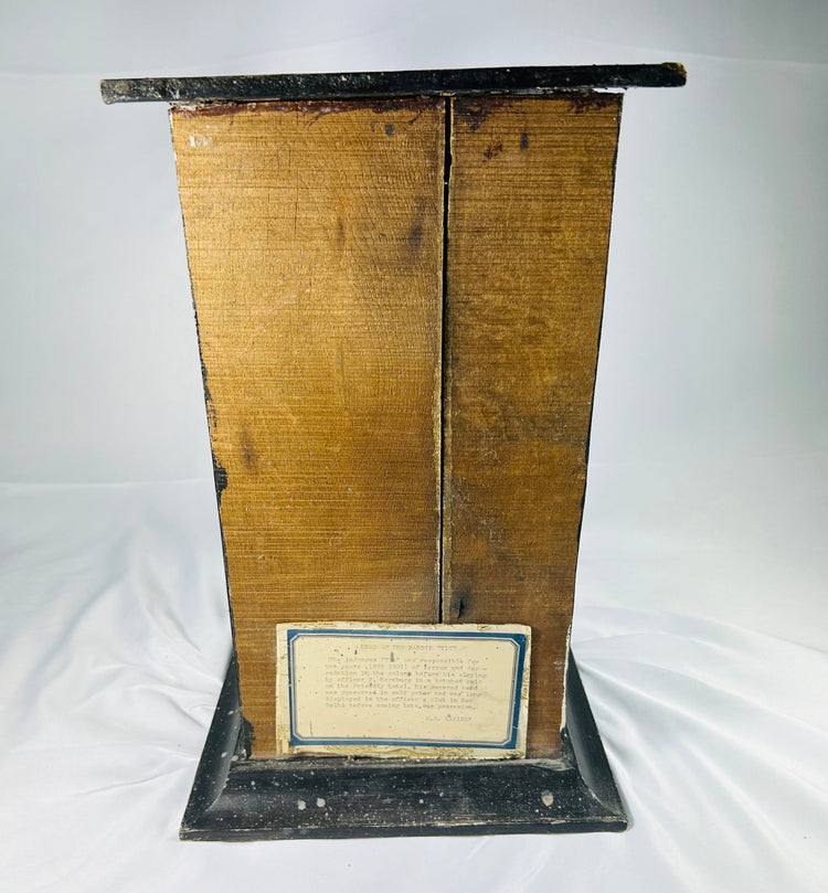 Rear view of 19th-century mummified head display case showing aged wooden backing and brass plaque with historical inscription on a white background.