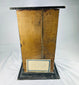 Rear view of 19th-century mummified head display case showing aged wooden backing and brass plaque with historical inscription on a white background.