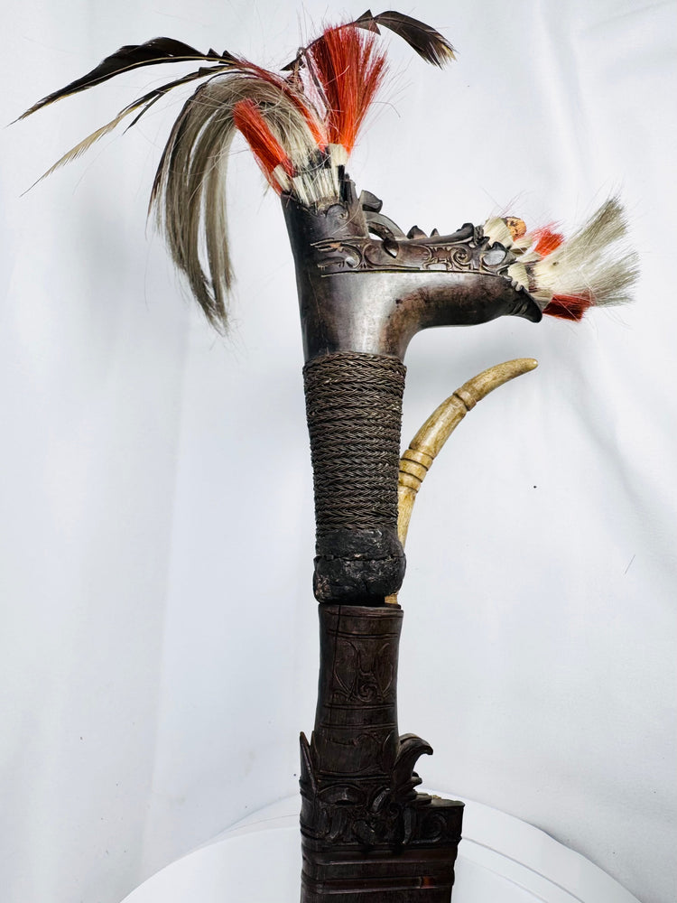 Side view of carved Mandau handle with curved decorative crest and attached feathers