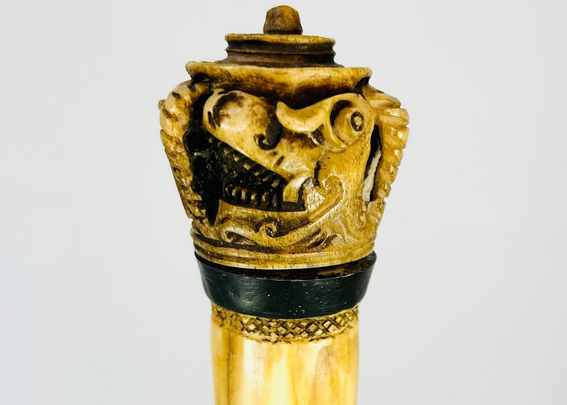 Indonesian Dayak knife from 19th century with carved bone handle depicting an Aso guardian beast and a male figure with elaborate mustache, steel blade, patinated surface, reflecting ritual and cultural significance of Borneo craftsmanship.