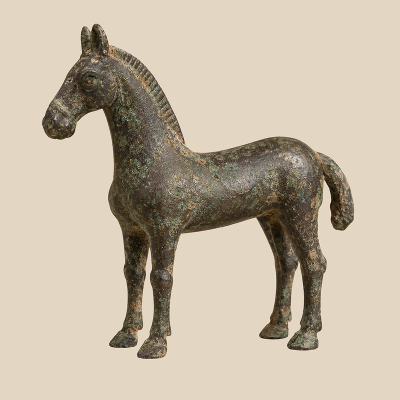 Bronze horse statuette with a dark brown surface, green patina and soil-like deposits against a warm ivory background.