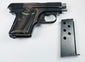 Browning Model 1906 pocket pistol beside a detached metal magazine with circular inspection holes.