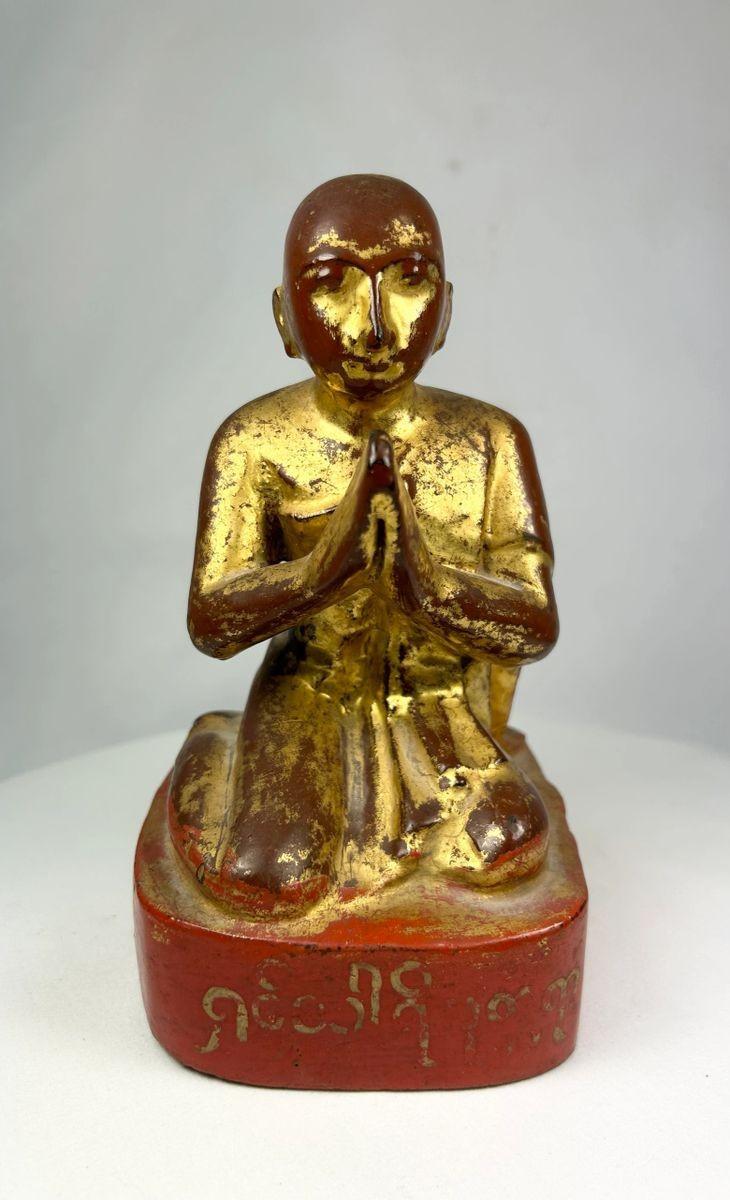 19th-century Burmese wooden monk statue with gold leaf and lacquer remnants, kneeling in Anjali Mudra with serene expression and inscribed base.