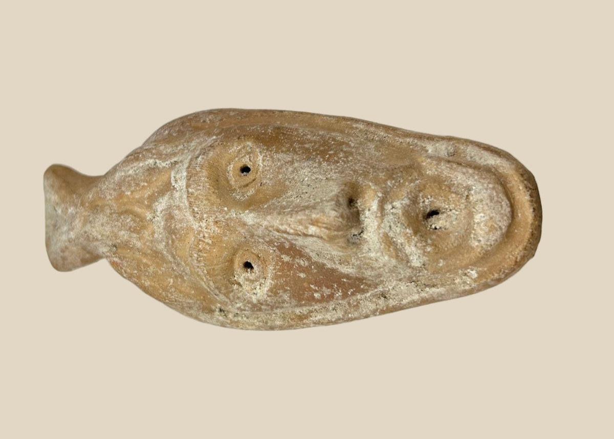 Ancient Byzantine terracotta oil lamp featuring a molded human face with open mouth spout, dating from the 5th to 7th century AD, showing aged surface encrustations.