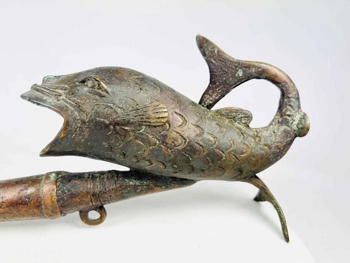 Antique Cameroonian bronze pipe in the form of a fish, early to mid 20th century, cast with detailed scales and curved tail, symbolic of fertility and abundance, shown against a white background.
