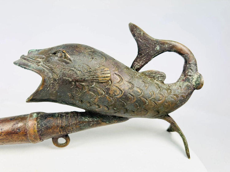 Antique Cameroonian bronze pipe in the form of a fish, early to mid 20th century, cast with detailed scales and curved tail, symbolic of fertility and abundance, shown against a white background.