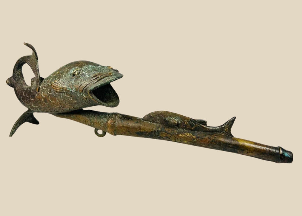 Antique Cameroonian bronze pipe in the form of a fish, early to mid 20th century, cast with detailed scales and curved tail, symbolic of fertility and abundance, shown against a white background.