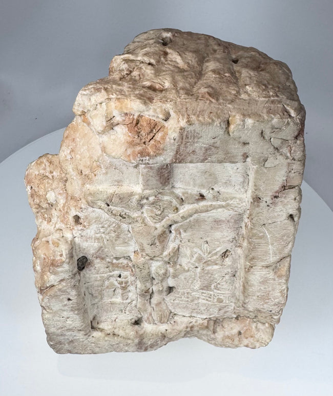 Weathered carved stone religious fragment featuring Christ crucified in medieval devotional style