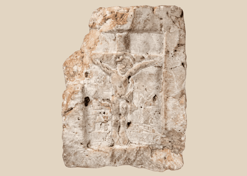 Medieval carved stone fragment depicting Christ on the Cross within an architectural niche with surrounding relief details