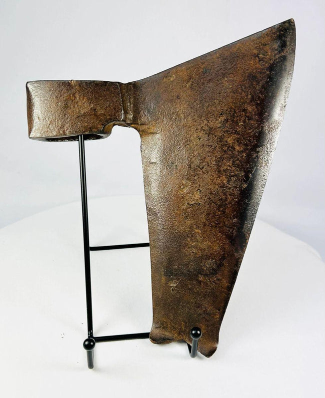 Aged metal goosewing axe head with textured rusted surface on black wire stand