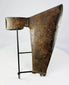 Aged metal goosewing axe head with textured rusted surface on black wire stand
