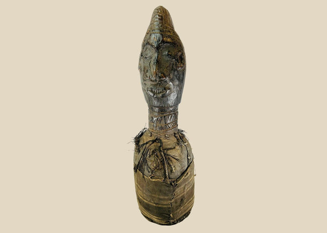 Hand-carved Central or West African wooden figure with elongated facial features, natural fiber torso wrapping, and traces of organic pigments, standing on a white background.