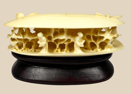 Front-facing view of a Chinese carved bone clam shell miniature with deep undercut interior figures on a dark wooden stand.