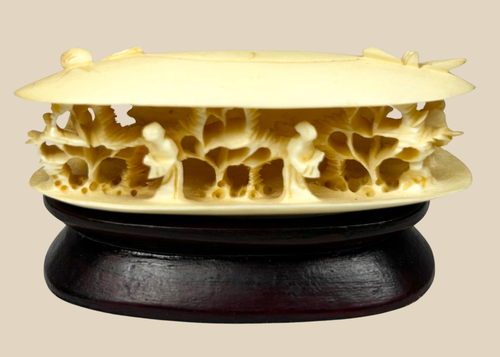 Front-facing view of a Chinese carved bone clam shell miniature with deep undercut interior figures on a dark wooden stand.