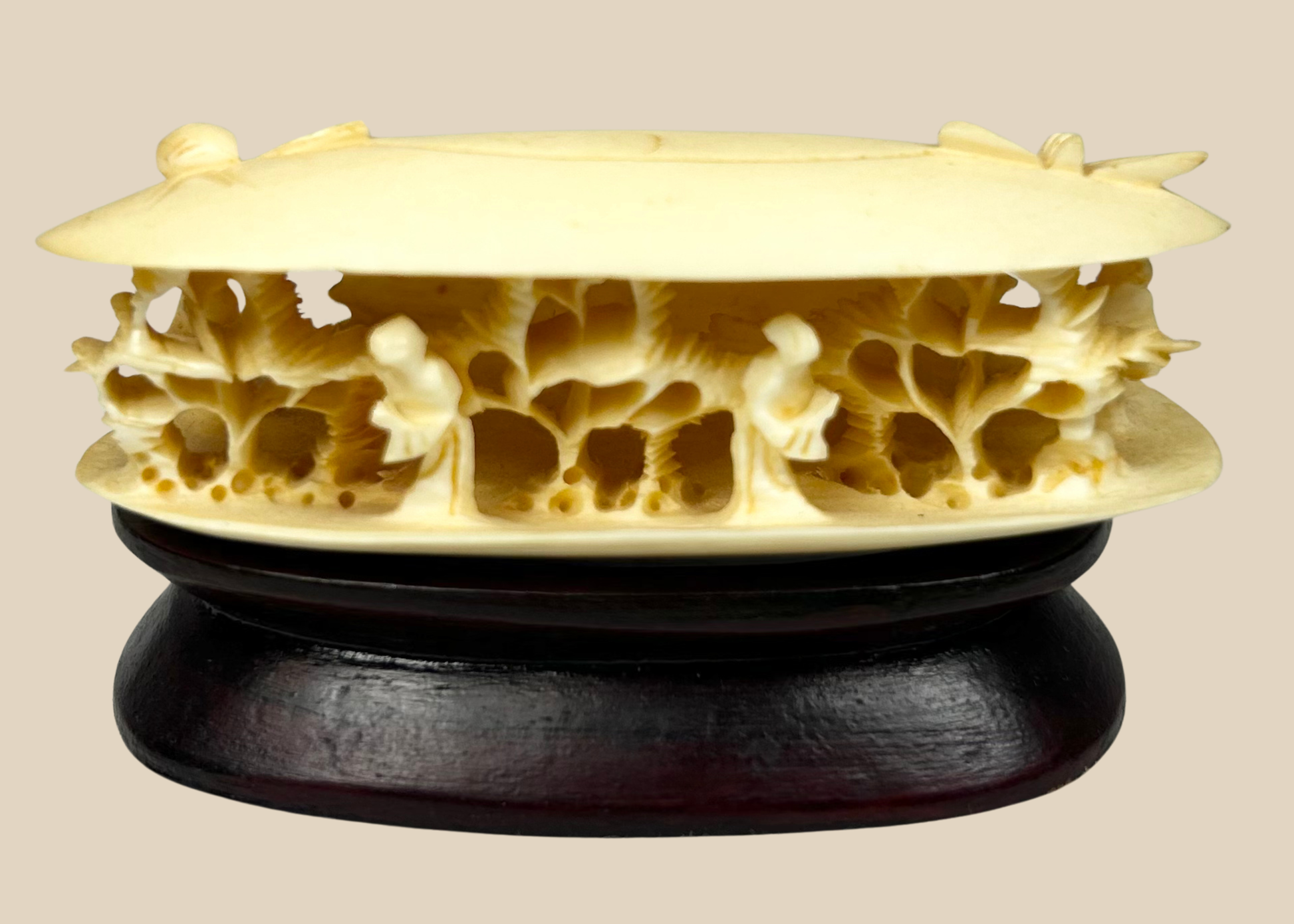 Front-facing view of a Chinese carved bone clam shell miniature with deep undercut interior figures on a dark wooden stand.