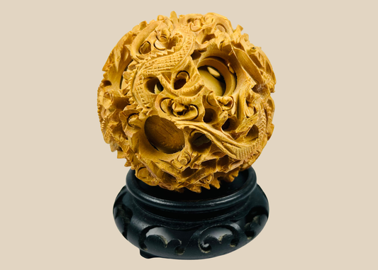 Ancient Chinese carved puzzle ball with dragon and cloud motifs on a black wooden stand against a beige background.