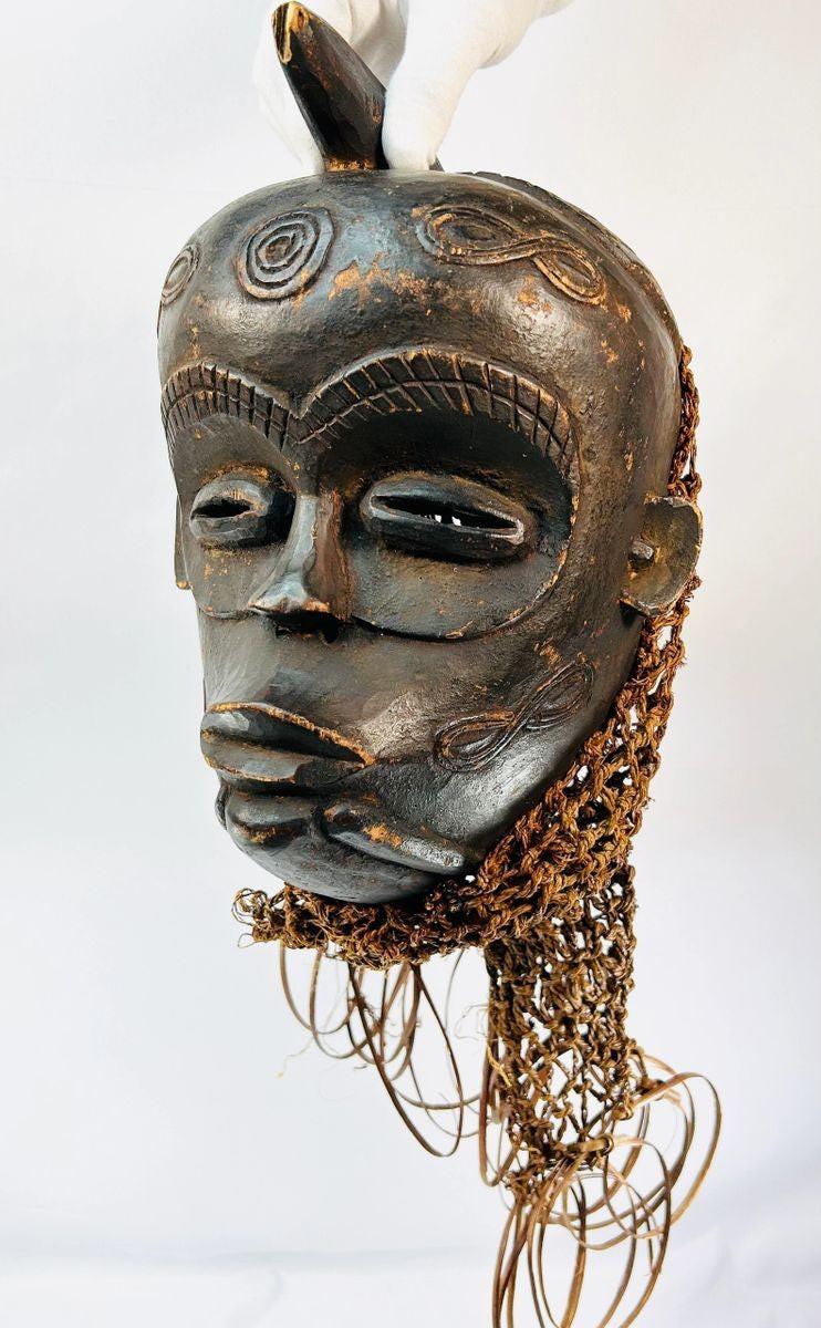 Chokwe wooden ceremonial mask from Central Africa with serene closed eyes, geometric forehead motifs, and wickerwork fiber adornments, 19th–20th century CE.
