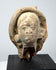 Classical antiquity terracotta head with softly modeled facial features and traces of an ancient headdress or head covering.