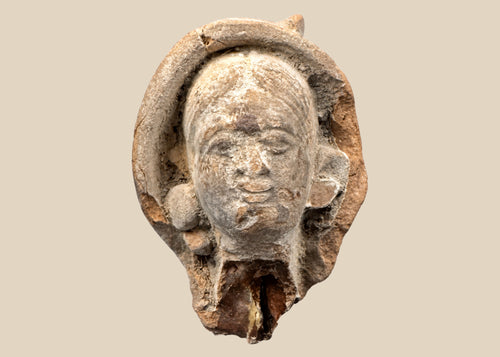 Terracotta head fragment from Classical Mediterranean, likely Greek or Roman, 1st Millennium BCE–CE. Features serene facial expression, partially preserved headdress, and natural weathered patina. Mounted on a custom stand, reflecting classical ideals of beauty, spirituality, and symbolic status in ancient art.