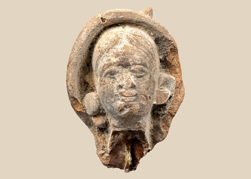 Terracotta head fragment from Classical Mediterranean, likely Greek or Roman, 1st Millennium BCE–CE. Features serene facial expression, partially preserved headdress, and natural weathered patina. Mounted on a custom stand, reflecting classical ideals of beauty, spirituality, and symbolic status in ancient art.