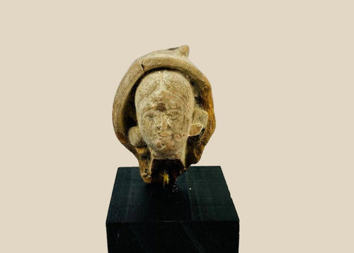 Terracotta head fragment from Classical Mediterranean, likely Greek or Roman, 1st Millennium BCE–CE. Features serene facial expression, partially preserved headdress, and natural weathered patina. Mounted on a custom stand, reflecting classical ideals of beauty, spirituality, and symbolic status in ancient art.