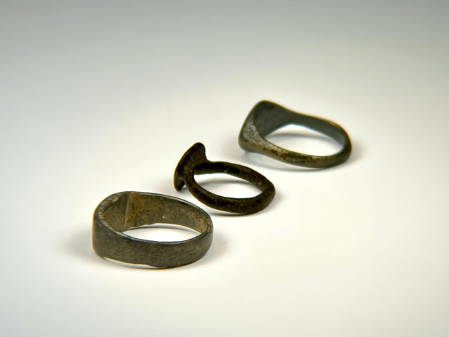 Three historic European bronze rings with engraved, shield-form, and plain band designs
