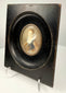 Three-quarter view of oval brass bezel on black ebonized art frame