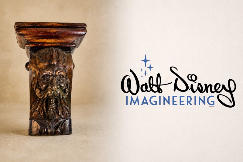 Historic carved architectural fragment displayed beside the Walt Disney Imagineering logo on a neutral museum-style background.