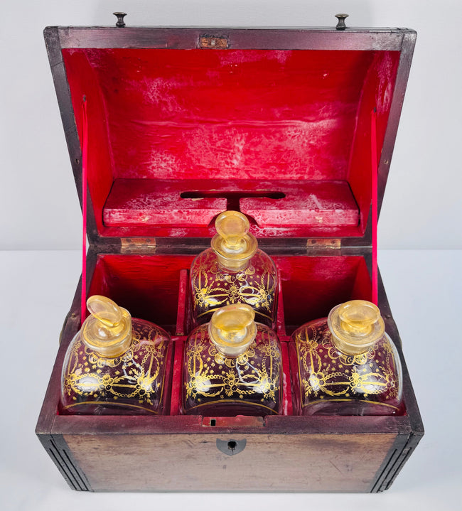 Open Georgian mahogany spirit box displaying four glass decanters, gilt decoration and rich red interior lining