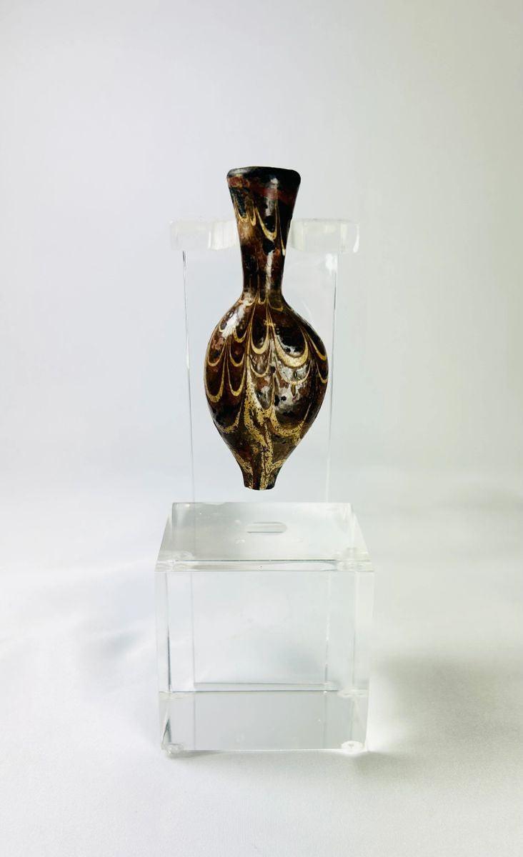 Ancient Eastern Mediterranean core-formed glass alabastron, 5th–6th Century AD, Late Roman to Byzantine period. Teardrop-shaped vessel with slender neck and pointed base, decorated with marbled browns, yellows, and gold, featuring delicate yellow trailing and swirling designs. Used for oils and perfumes, reflecting luxury, artistry, and status in antiquity.