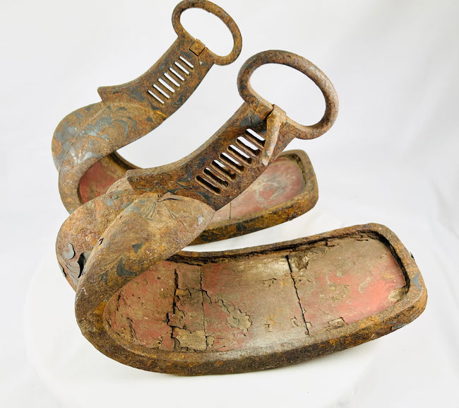 Antique Edo-period samurai stirrups with black and brown lacquer remnants and aged iron surfaces, shown as a matched pair.