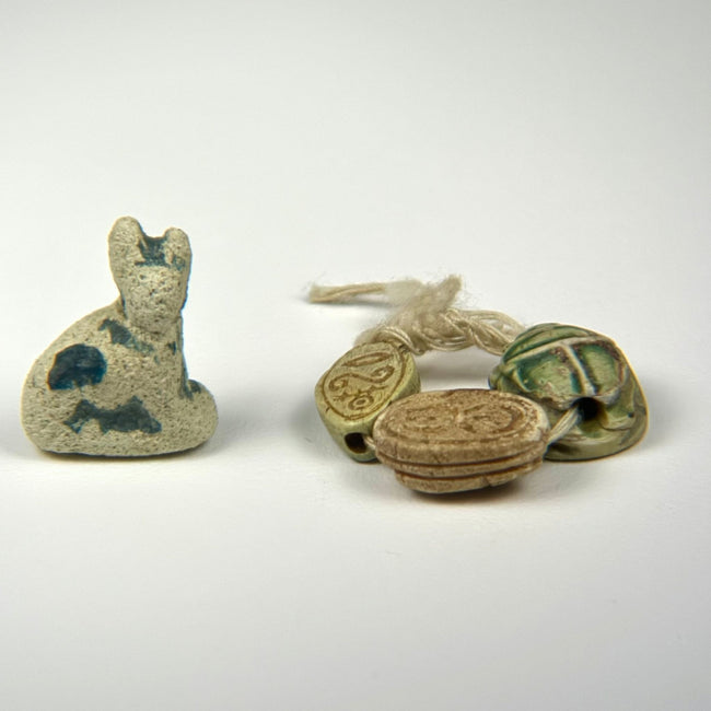 Ancient Egyptian amulet collection with seated Bastet cat and three scarabs in faience, steatite, and glazed composition.