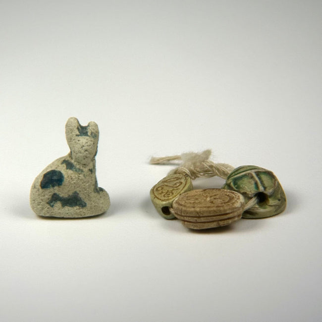 Side-by-side view of seated cat amulet and three stringed scarabs highlighting pale green glaze and blue accents