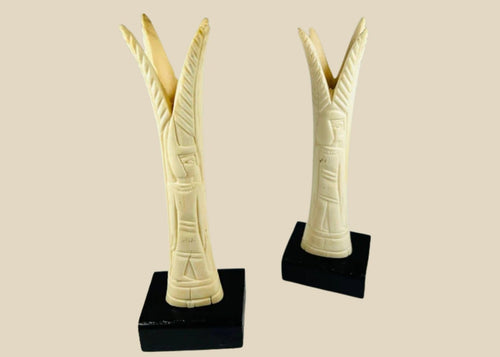 Pair of carved Egyptian ivory sistrum handles on black display bases, featuring stylized figures and decorative motifs, dating to the Third Intermediate Period, circa 1070–664 BCE.