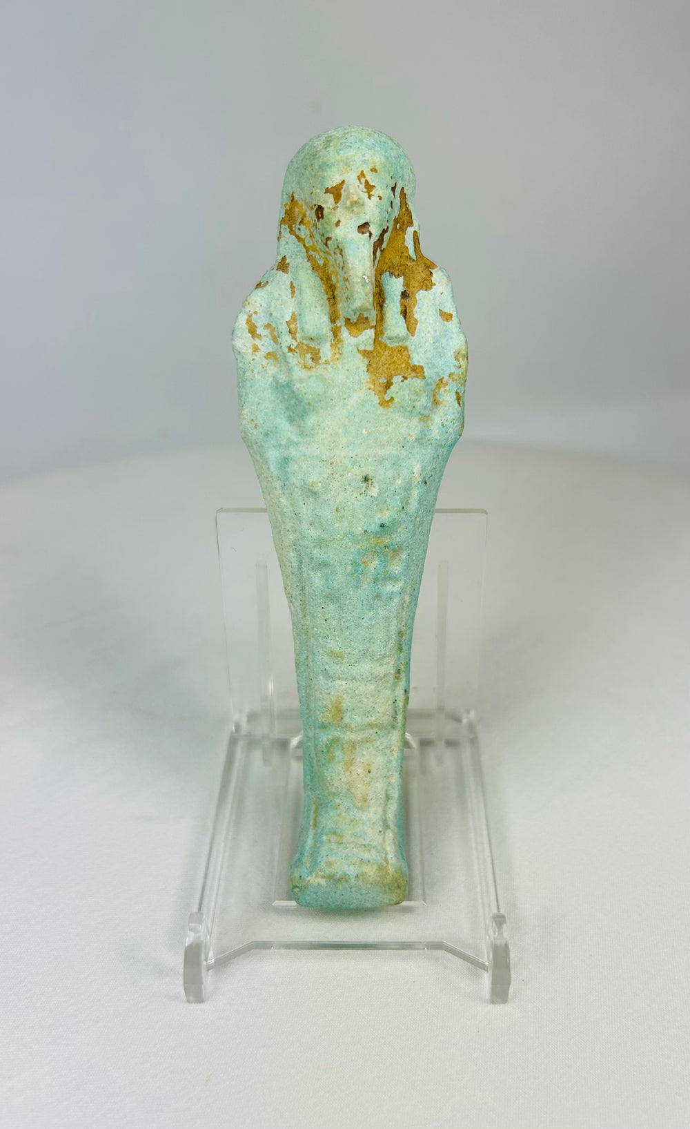 Ancient Egyptian turquoise-blue faience Ushabti standing on a clear display base against a white background