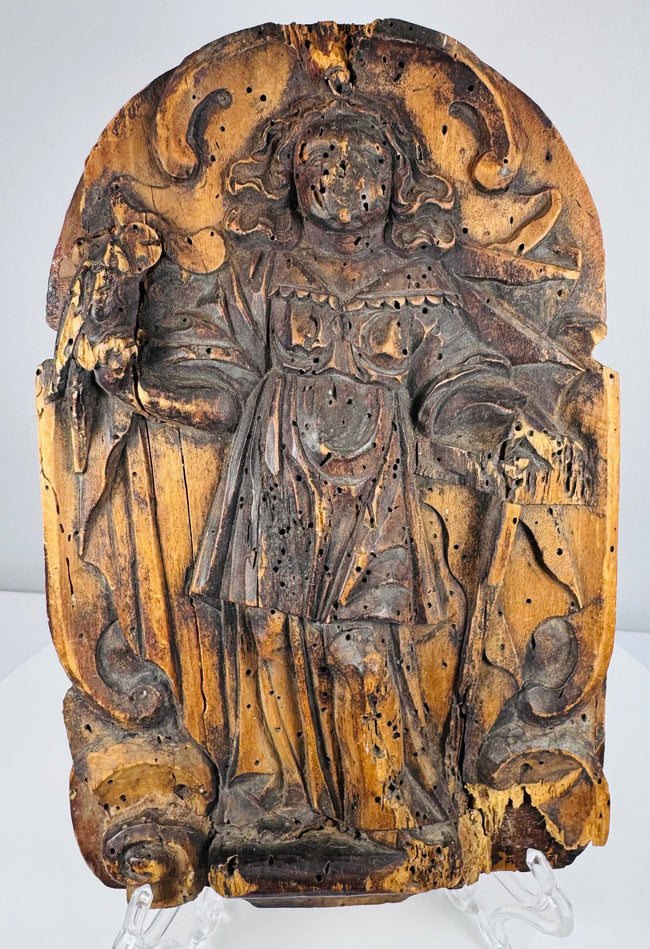 Close-up of an antique carved wooden saint with a circular halo and staff-like devotional attribute
