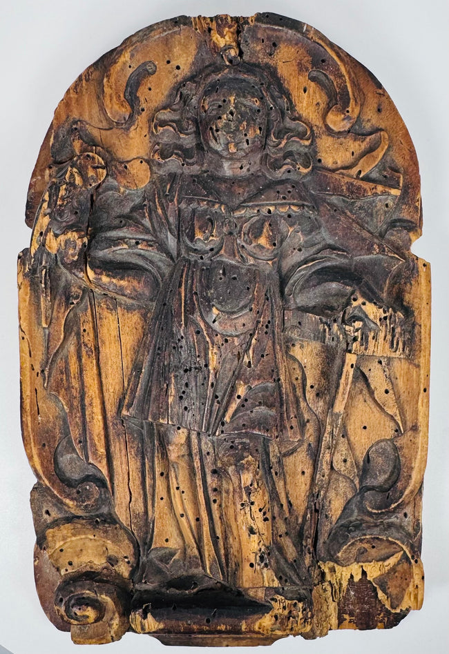 Weathered European religious wood carving with a robed saint beneath a rounded ornamental arch