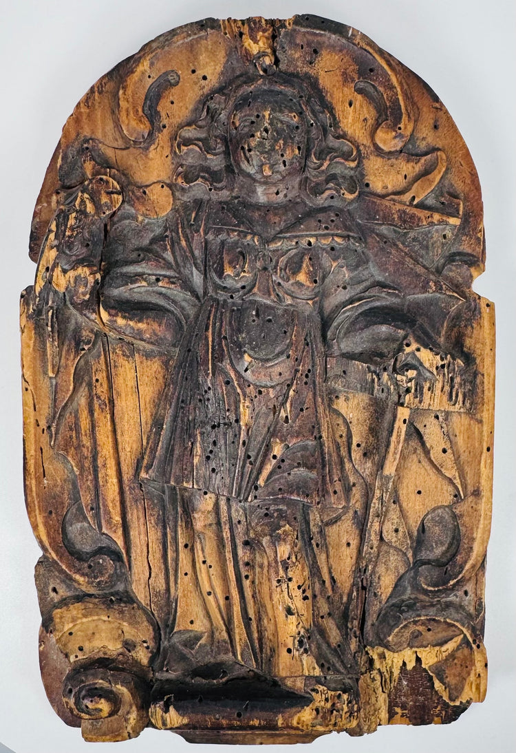Weathered European religious wood carving with a robed saint beneath a rounded ornamental arch