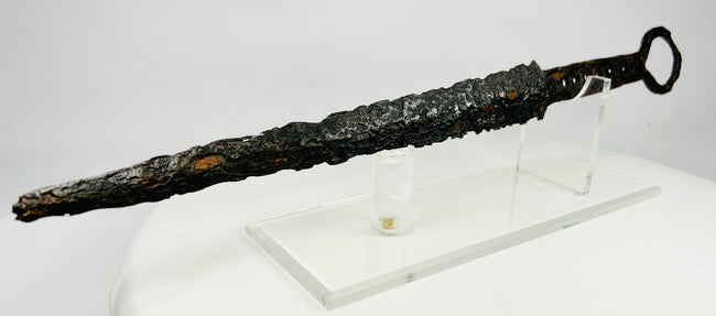 Medieval European dagger with ring pommel and corroded forged steel blade on acrylic display stand — 14th-century weapon artifact photographed on white background.