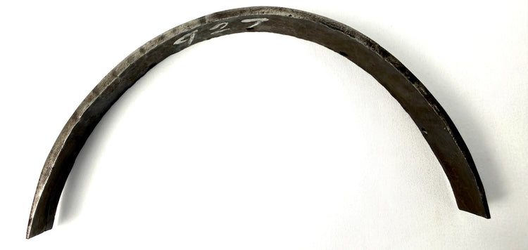 Curved steel band on white cloth showing arch shape, tapered ends, and inventory marking