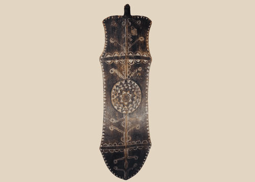 African carved wooden ceremonial shield with geometric decoration and central circular medallion